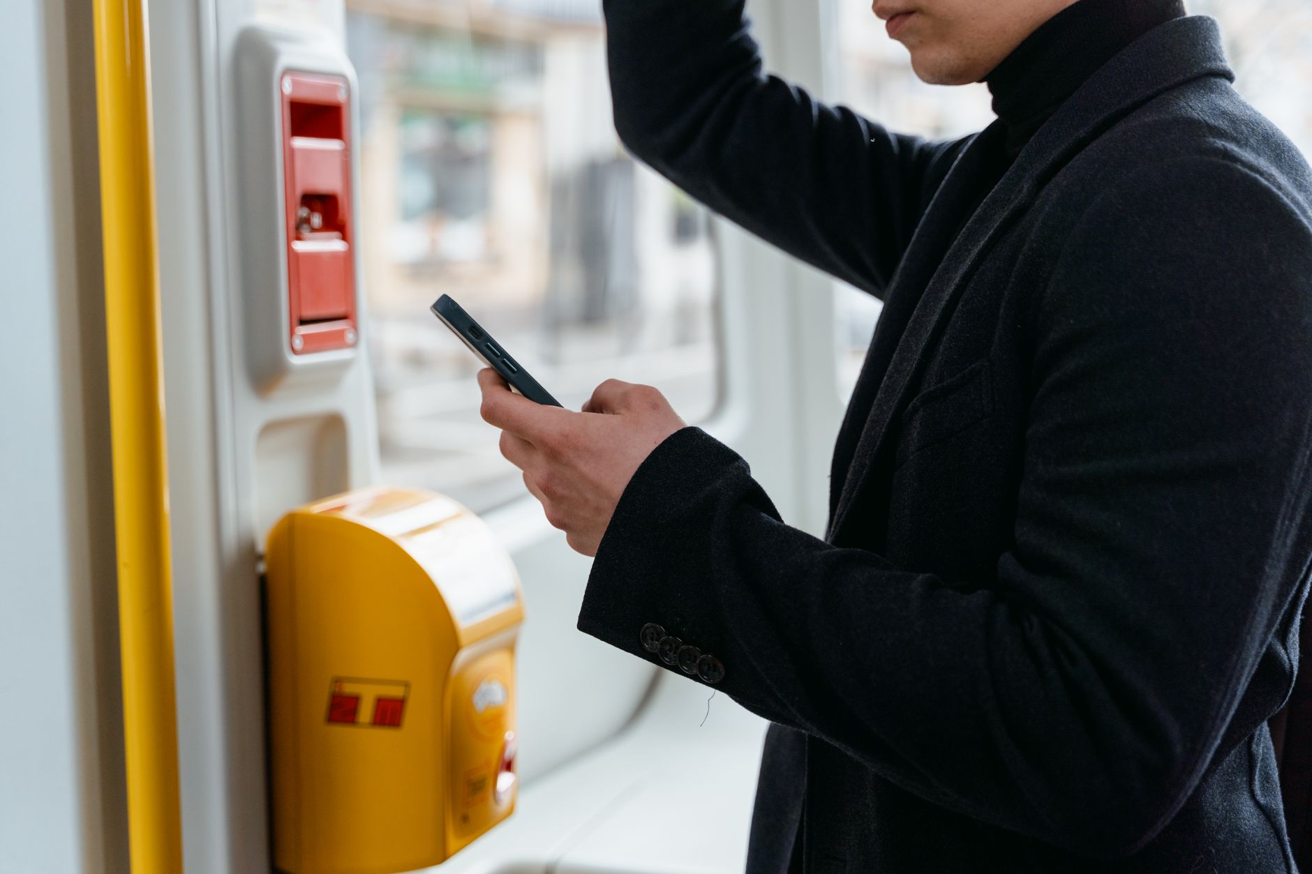 Un adulte en manteau noir vérifiant son smartphone en se déplaçant dans les transports en commun.