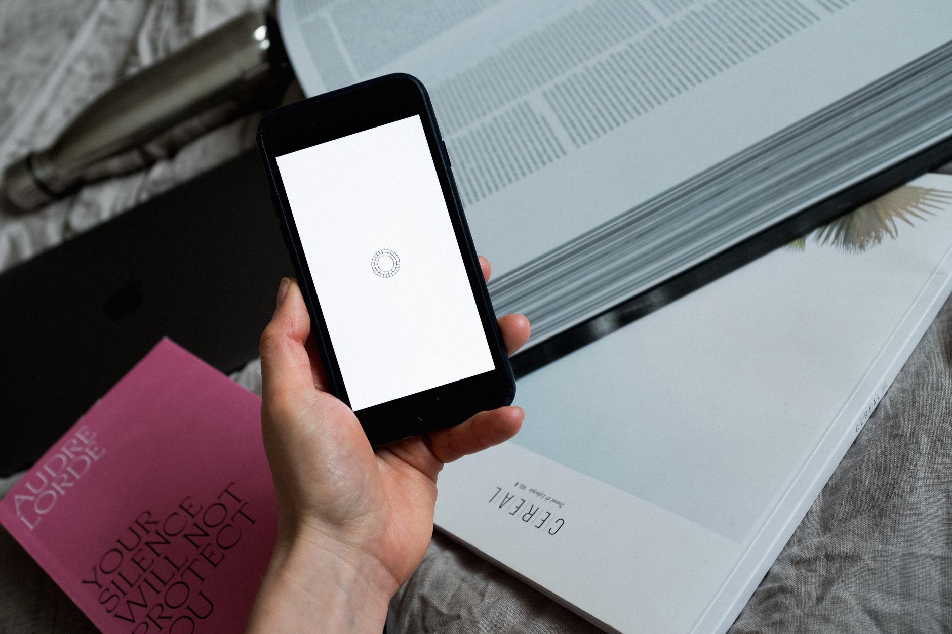Vue de dessus d'une personne anonyme montrant l'écran vierge d'un téléphone portable avec un symbole de chargement, le gadget étant près d'un livre ouvert posé sur une feuille
