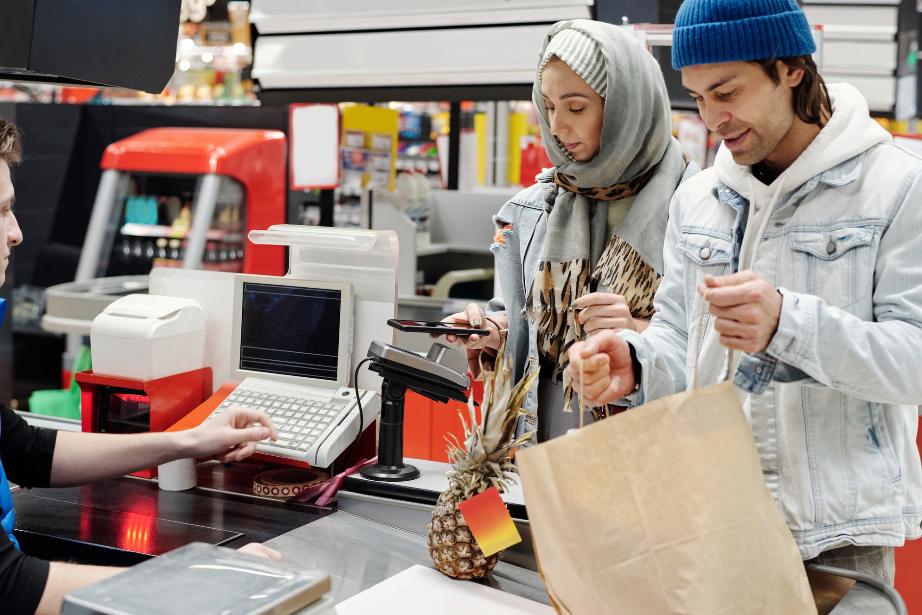 Un couple du Moyen-Orient effectuant un achat à la caisse d'un supermarché à l'aide d'un smartphone.