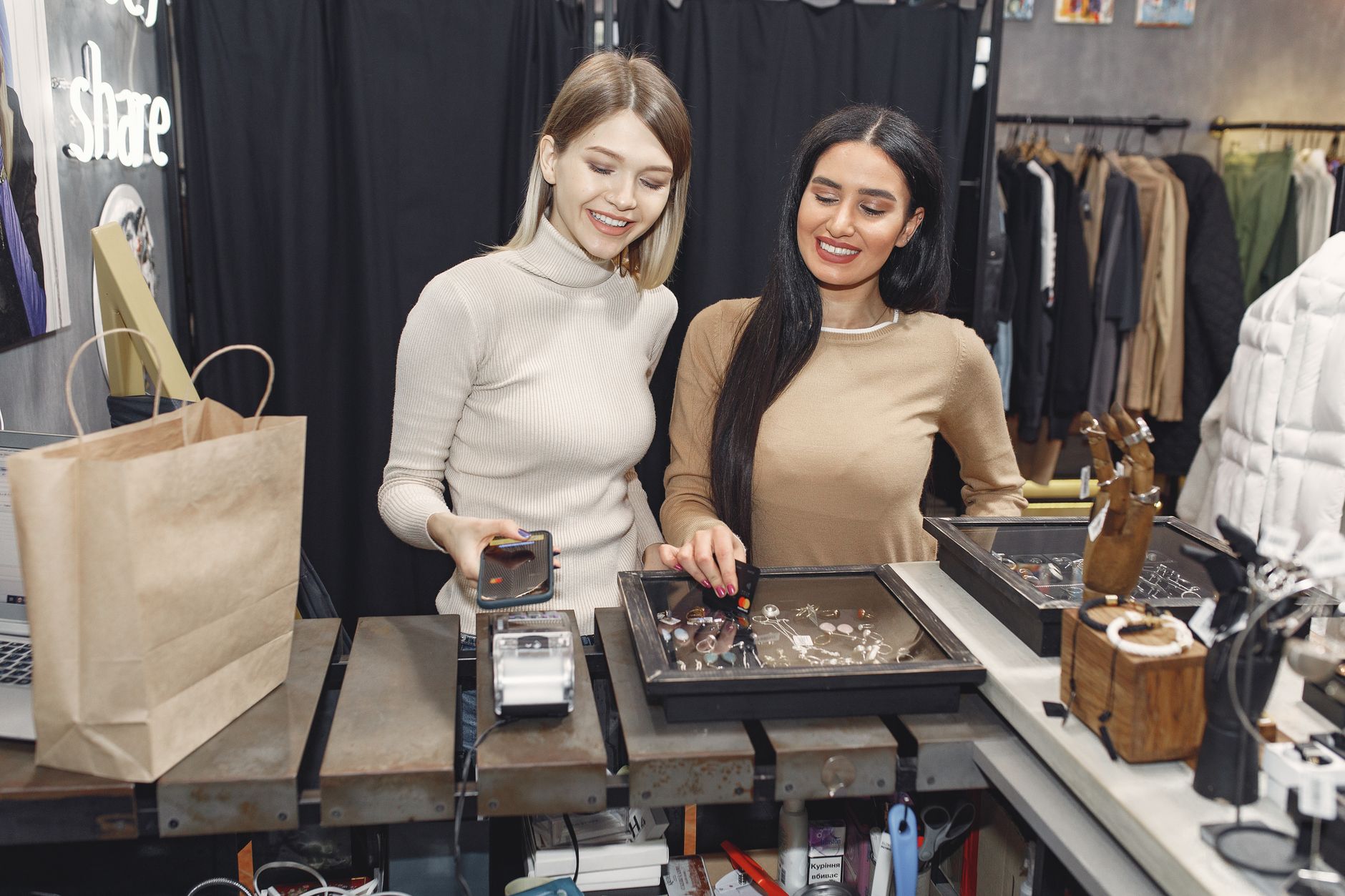 Femmes joyeuses habillées décontractées payant avec un smartphone et une carte de crédit pour des achats en se tenant près d'un terminal sans contact au comptoir