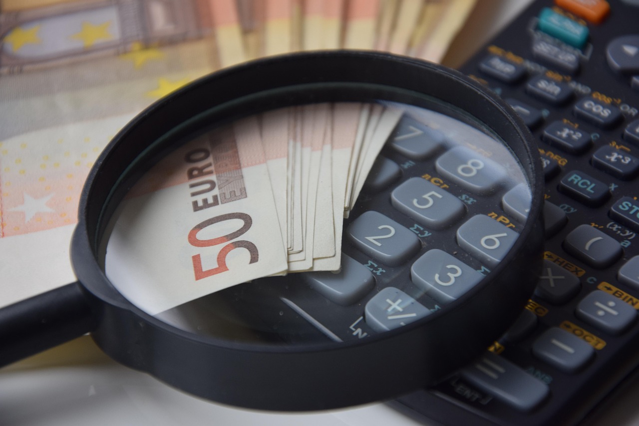 Loupe posée sur des billets en euros à côté d’une calculatrice