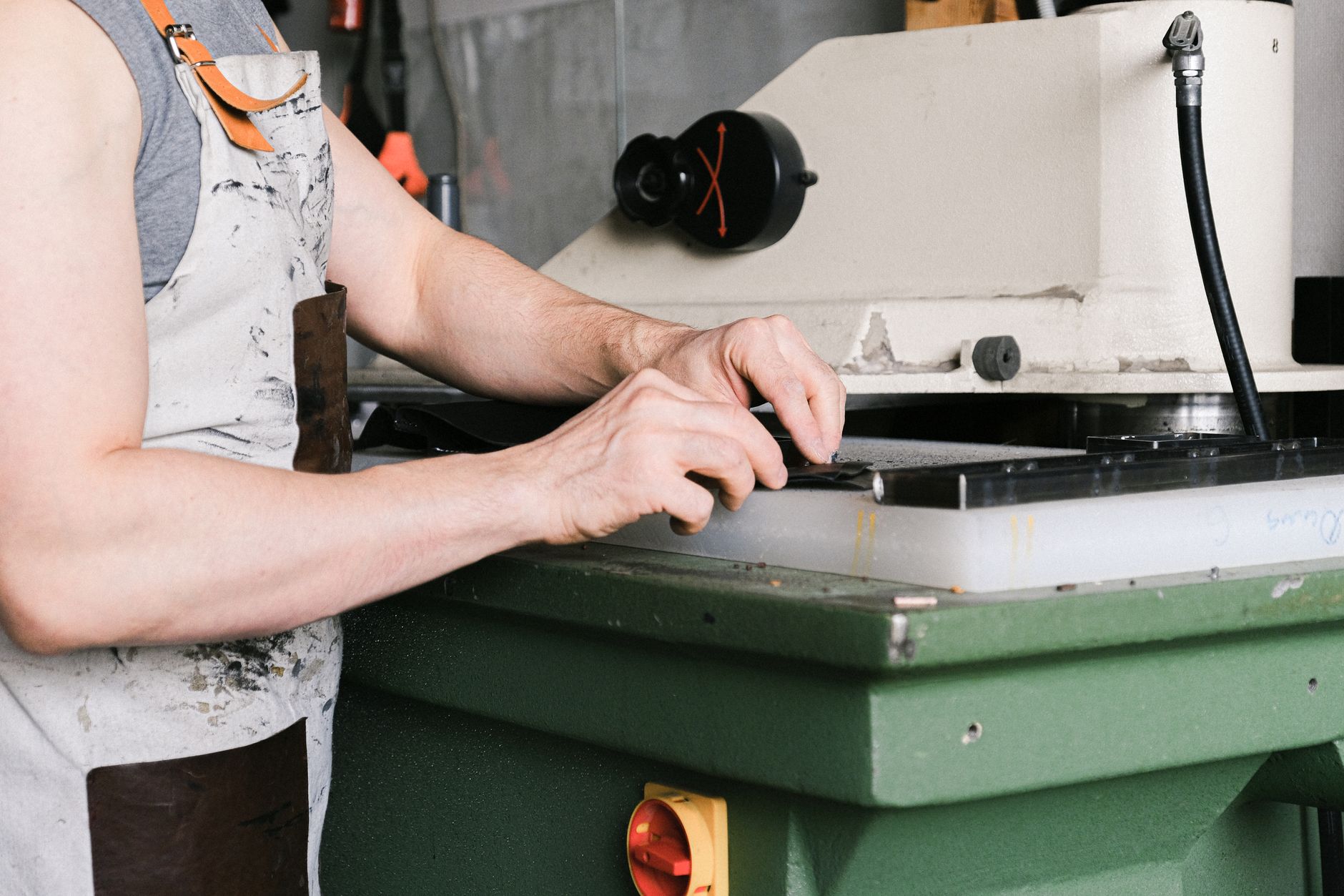 Mains d’un opérateur en tablier posant une pièce sombre sur le plateau d’une machine industrielle verte dans un atelier.
