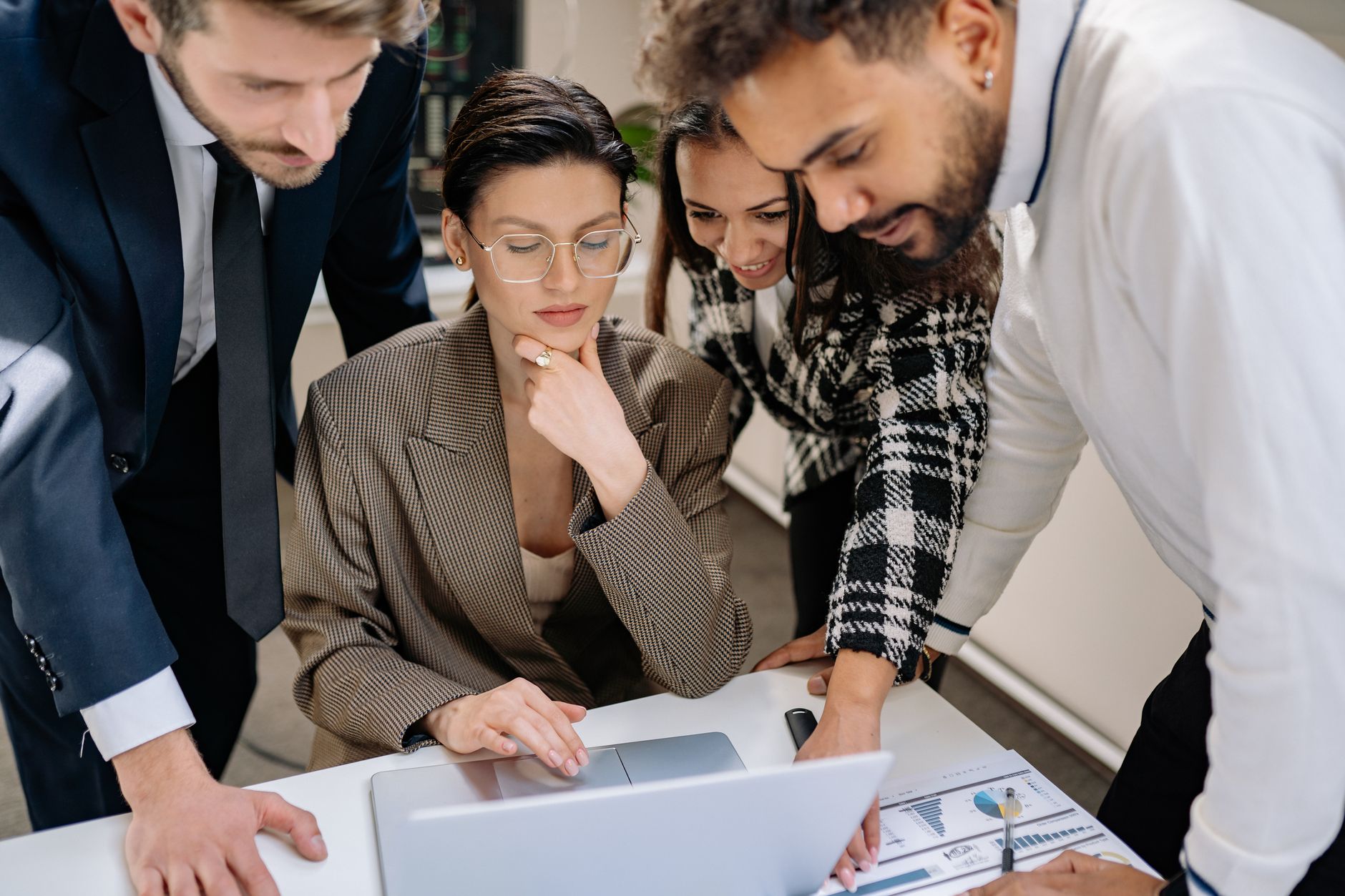Quatre collègues réunis autour d’un ordinateur portable sur un bureau, avec des documents à graphiques posés sur la table.
